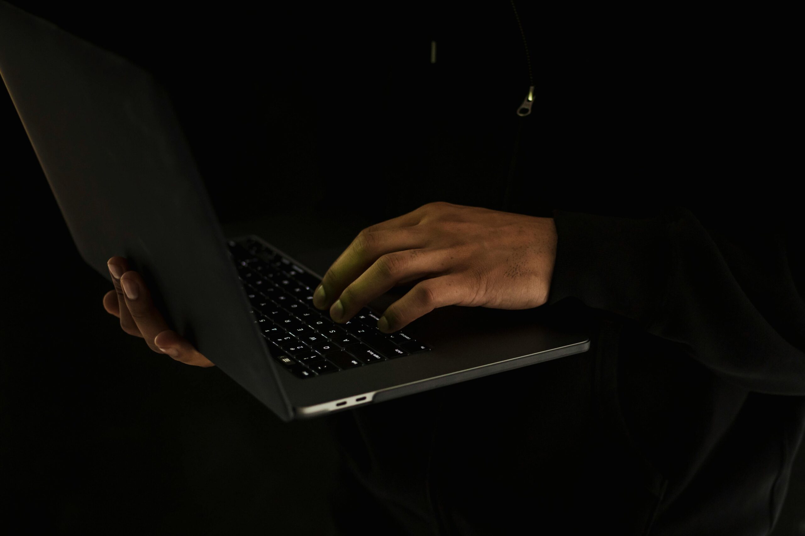 Crop unrecognizable man using laptop in darkness